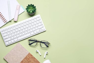 Kulaklıklı bilgisayar klavyesi, gözlük ve açık yeşil arka planda ofis kırtasiyesi.
