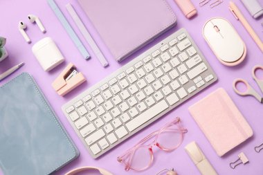 Fare kulaklıklı bilgisayar klavyesi ve eflatun arkaplanlı ofis kırtasiyesi