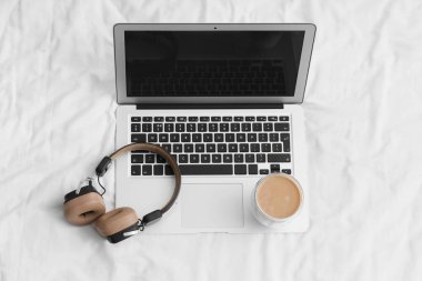 Yatağında kahve ve kulaklık olan bir laptop.