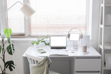 Ofisin penceresinin yanında dizüstü bilgisayarı, tableti ve kulaklığı olan modern işyeri