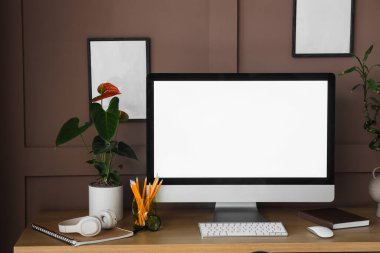 Ofisteki kahverengi duvarın yanında modern bilgisayarı, çiçekleri ve fotoğraf çerçeveleri olan şık bir iş yeri.