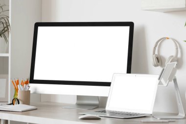 Ofiste beyaz duvarın yanında bilgisayar, dizüstü bilgisayar ve kulaklık bulunan modern işyeri