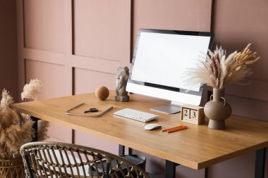 Ofisteki kahverengi duvarın yanında bilgisayarı, otlağı ve takvimi olan modern işyeri