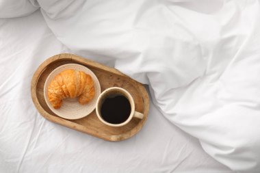 Bir fincan kahve ve beyaz çarşaflı kruvasan.