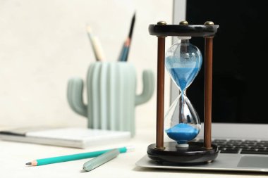 Ofisteki beyaz masada dizüstü bilgisayarı ve kırtasiyesi olan kum saati.