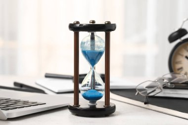 Ofisteki beyaz masada dizüstü bilgisayarı, defterleri ve gözlükleri olan kum saati.