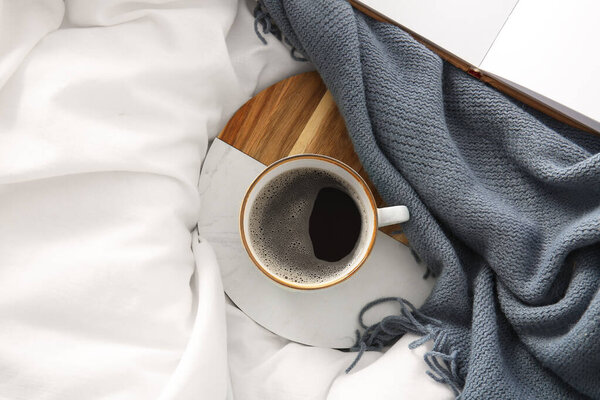 Поднос с чашкой кофе, одеяло и книга на белых простынях