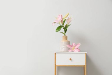Gri arka planda vazoda güzel çiçekler olan beyaz komodin.