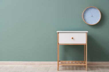 Beyaz komodin ve saat yeşil duvarda asılı.