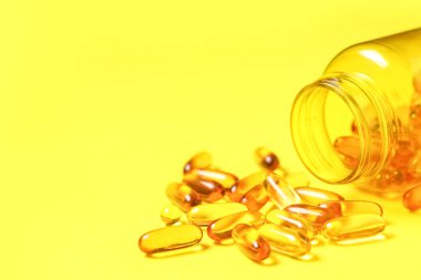 Sarı zemin üzerinde E vitamini kapsülleri olan kavanoz