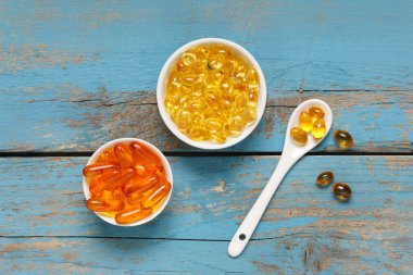 Mavi ahşap arka planda E vitamini hapları olan kaseler, yakın plan.