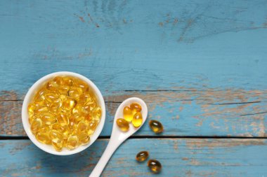Mavi ahşap arka planda E vitamini haplı kase ve kaşık, yakın plan.