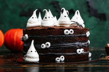 Tatlı Cadılar Bayramı pastası, yeşil arka planda siyah ahşap masada hayaletlerle süslenmiş.