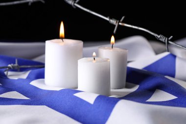 İsrail bayrağında yanan mumlar ve dikenli teller koyu arka planda. Uluslararası Soykırım Anma Günü