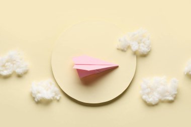 Açık sarı arka planda, güneş ve pamuk kaplı pembe kağıt uçak.