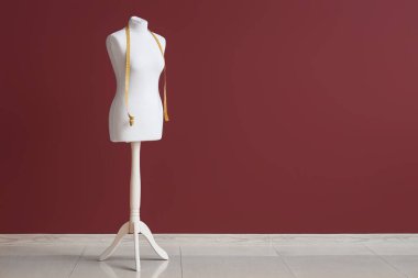 Koyu kırmızı duvarın yanında mezurası olan terzi mankeni.