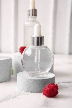 Beyaz arka planda kozmetik ahududu yağı şişeleriyle dekoratif podyumlar