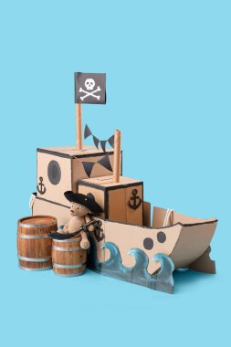 Mavi arka planda oyuncak ayı ve varilleri olan korsan karton gemi.