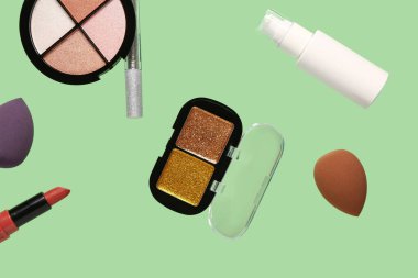 Yeşil arka planda uçan dekoratif kozmetik ürünleri