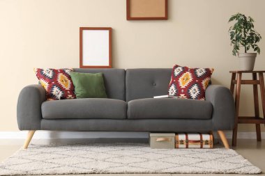 Oturma odasının içinde siyah kanepe, yastıklar, resimler ve çiçek var.