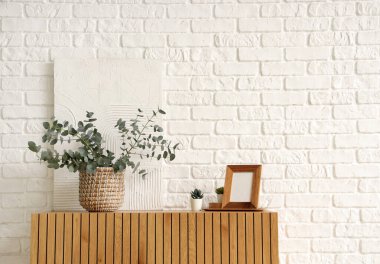 Taze okaliptüs dallı vazo ve beyaz tuğla duvarın yanındaki çekmecelerin üzerindeki çerçeve.