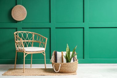 Hasır koltuk ve sepet, yeşil duvarın yanında çiçek var.