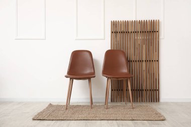 Modern kahverengi sandalyeler ve beyaz duvarın yanındaki ahşap ekran.