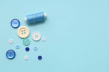 Mavi zemin üzerinde iğne ve farklı düğmeler olan iplik makarası