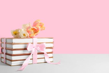Pembe kurdeleli bir yığın kitap ve renkli arka planda güzel lale çiçekleri.