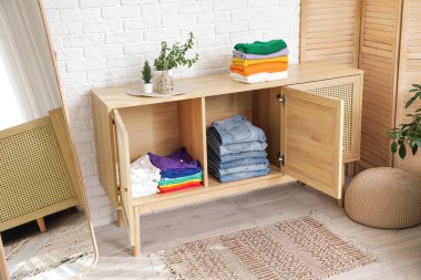 Giysileri, aynası ve beyaz tuğlalı duvarın yanında katlanan bir elbise.