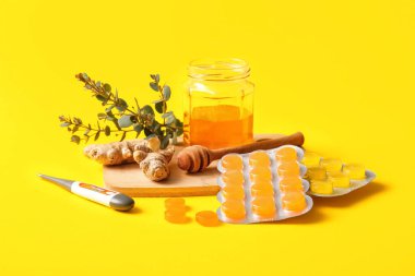 Öksürük damlaları zencefil, termometre ve sarı arka planda bal ile su topluyor.