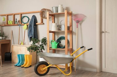 Bahçıvan çalışma alanı, raf ünitesi, el arabası ve ışık duvarı yakınında farklı bahçe malzemeleri.