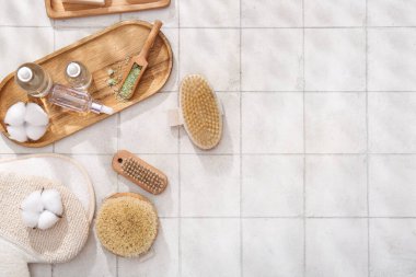 Beyaz karo arka planda eldiven, kozmetik ürünleri ve pamuk çiçekleriyle masaj fırçaları