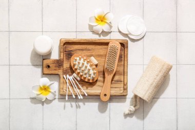 Pamuklu masaj fırçaları, kozmetik ürünleri ve beyaz karo arka planda tesisat çiçekleri