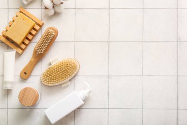 Beyaz fayans zemininde kozmetik ürünleri, sabun ve pamuk çiçekleri ile masaj fırçaları