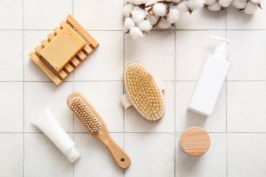 Beyaz fayans zemininde kozmetik ürünleri, sabun ve pamuk çiçekleri ile masaj fırçaları