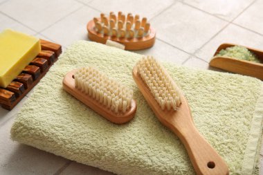 Beyaz fayans zemininde havluyla masaj fırçaları, deniz tuzu ve sabun, yakın plan