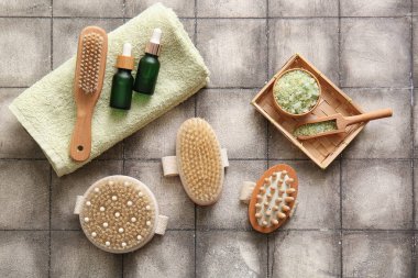 Havluyla masaj fırçaları, kozmetik ürünleri ve gri fayans üzerinde deniz tuzu