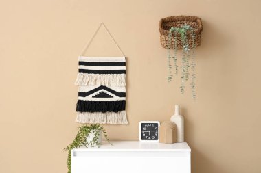 Oturma odasında bej duvarın yanında saati ve bitkisi olan çekmeceler, yakın plan.