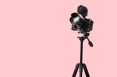 Pembe arka planda tripodun üzerinde profesyonel kamera