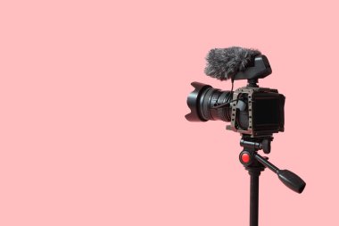 Pembe arka planda tripodun üzerinde profesyonel kamera, yakın plan.
