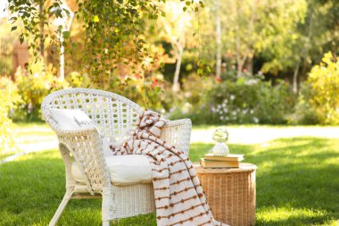 Rahat beyaz hasır koltuk battaniyeli ve kitaplarla parkta, açık havada kahve masasında.