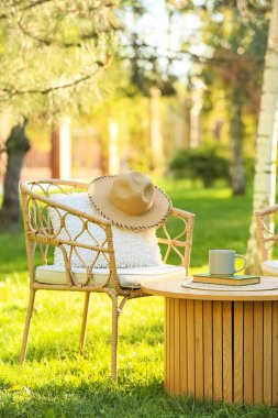 Rahat hasır koltuk, yastık, kitap ve kahve parktaki masada, açık havada.