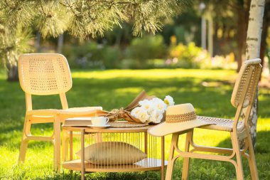 Kitaplı rahat hasır sandalyeler, parkta, açık havada bir fincan kahve ve buket.