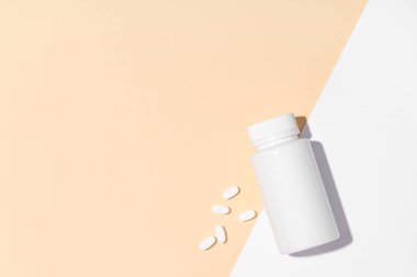 Boş plastik vitamin şişesi ve renkli arka planda beyaz haplar.