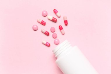 Boş plastik vitamin şişesi ve pembe arka planda farklı haplar.