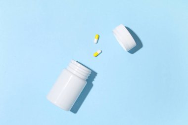 Boş plastik vitamin şişesi ve mavi arka planda haplar.