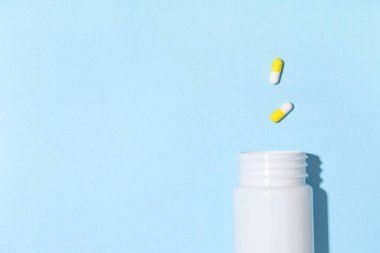 Boş plastik vitamin şişesi ve mavi arka planda haplar.