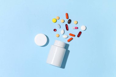 Boş plastik vitamin şişesi ve mavi arka planda farklı haplar.