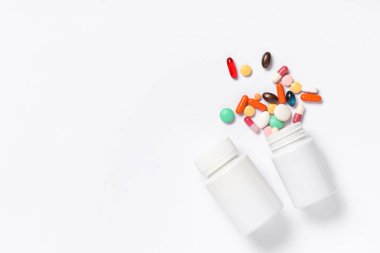 Gri arka planda farklı haplarla dolu boş plastik vitamin şişeleri.